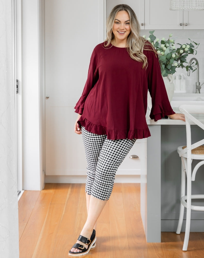 Woman wearing a burgundy top and black and white checkered pants in a kitchen.