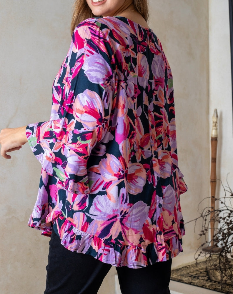 Woman wearing a colorful floral blouse with bell sleeves indoors.