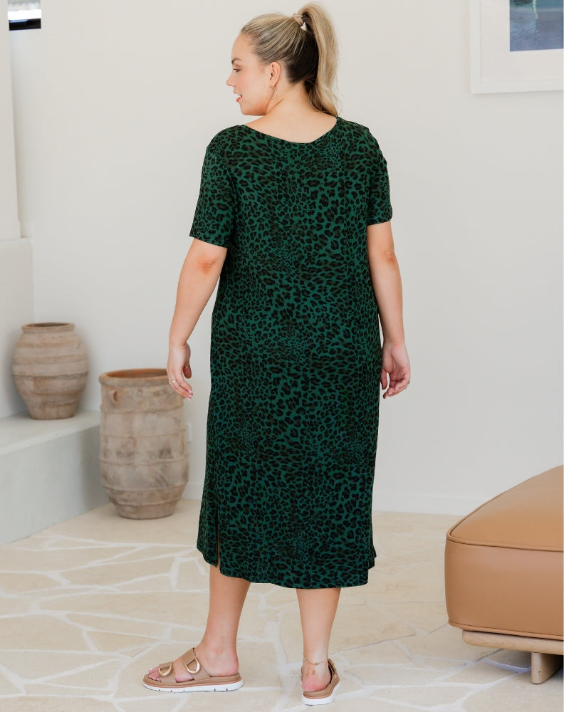 Woman wearing a green patterned dress standing in a room with neutral decor.