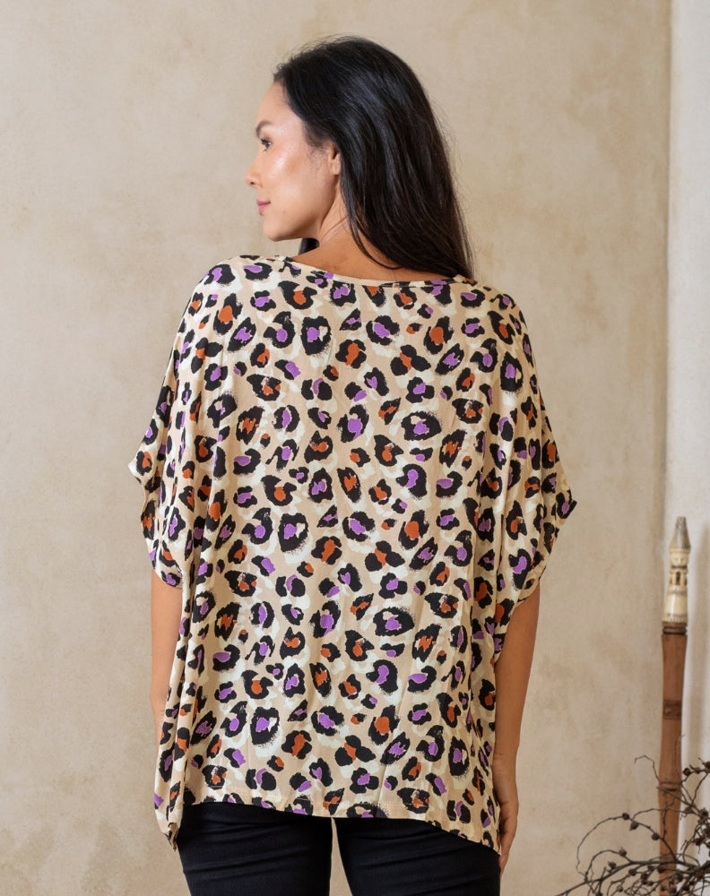Woman wearing a leopard print top against a beige wall.