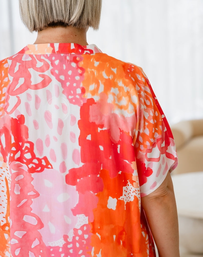 Person wearing a colorful kimono-style garment with abstract patterns in orange, pink, and white.