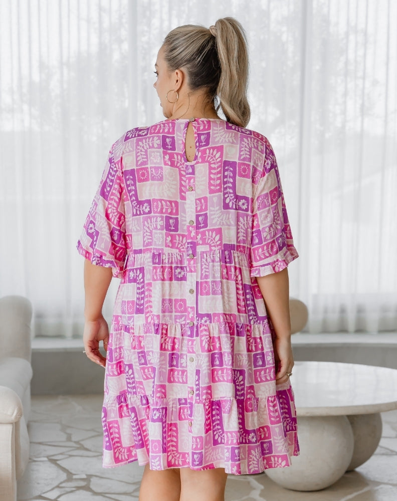Woman wearing a pink and white patterned dress in a bright room.