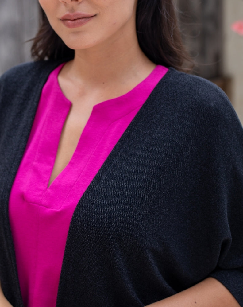 Close-up of a person wearing a black cardigan over a bright pink top.