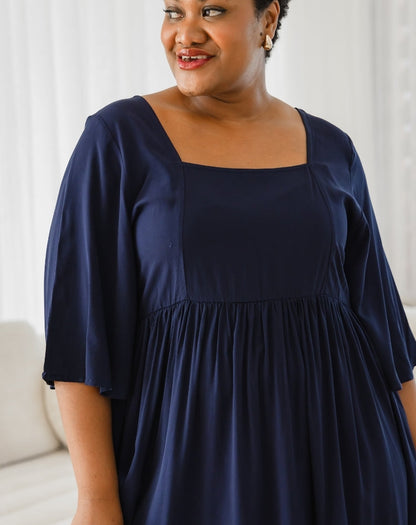 Woman wearing a navy blue dress against a white curtain background