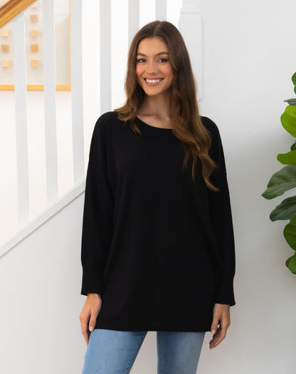 Woman wearing a black long tunic knit top and light blue jeans indoors.