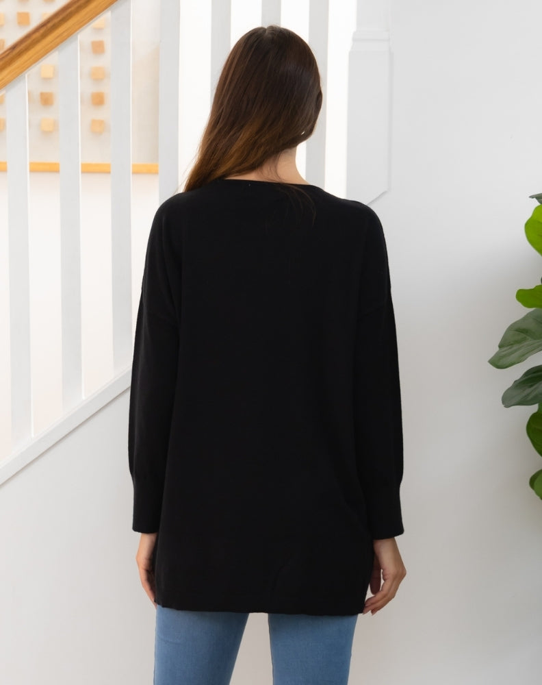 Person wearing a black tunic knit with a white wall and staircase in the background