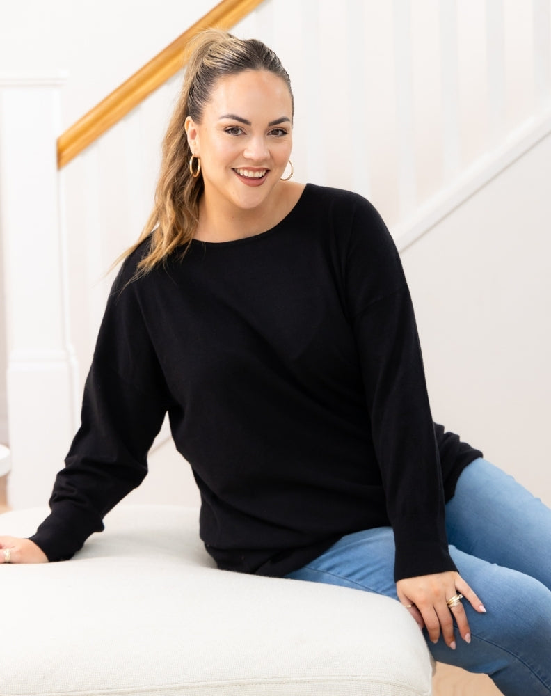 Woman wearing a black sweater and blue jeans sitting on a white couch.