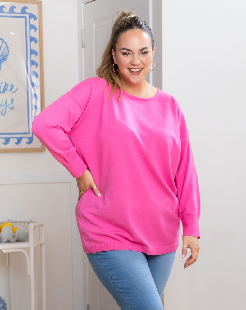 Woman wearing a bright pink sweatshirt and blue jeans indoors.