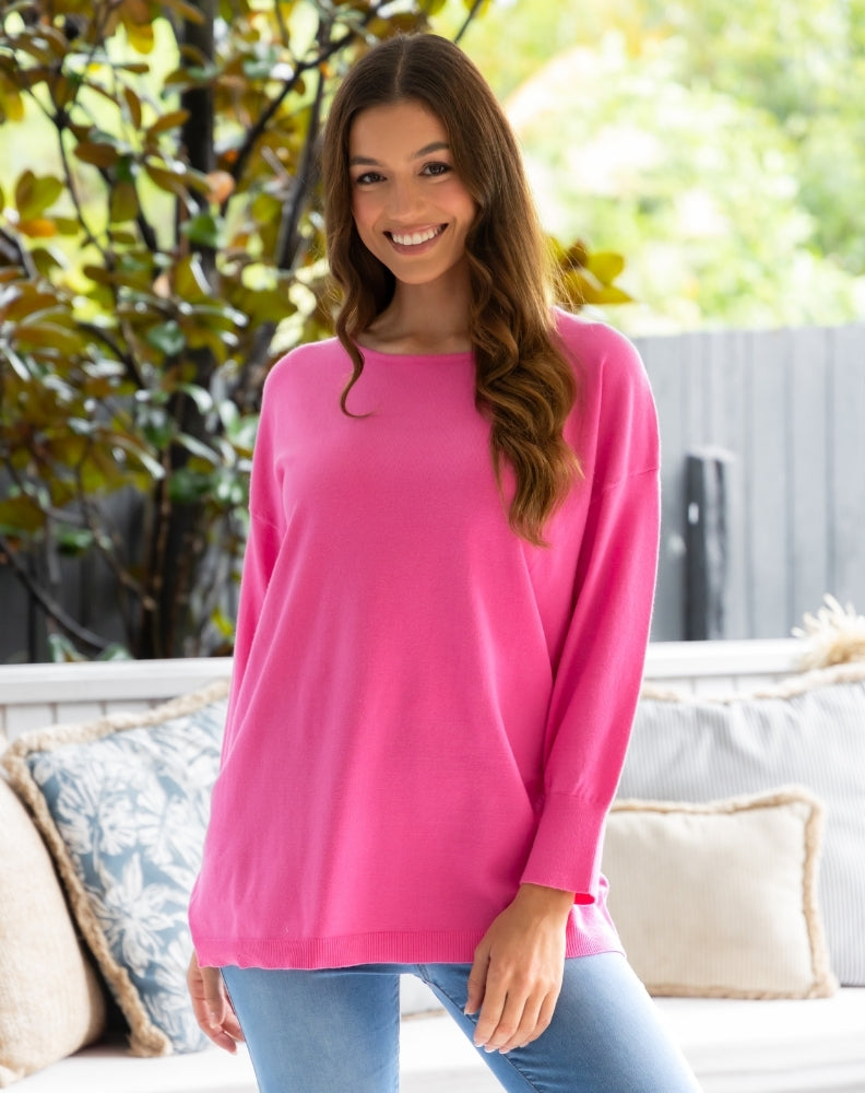 Woman wearing a pink sweater sitting on a couch outdoors.