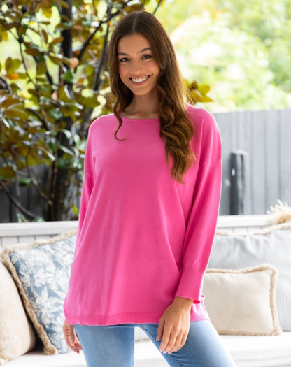 Woman wearing a pink sweater sitting on a couch outdoors.