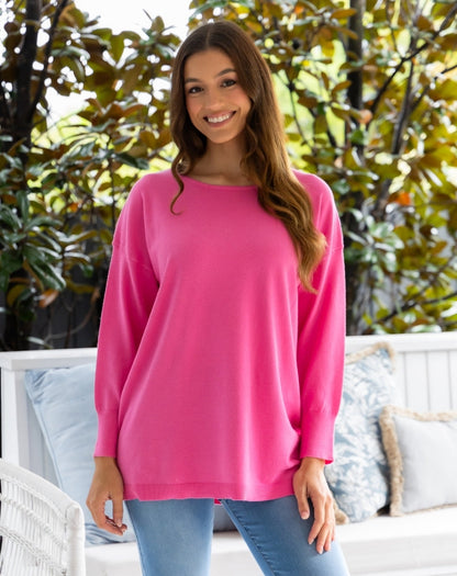 Woman wearing a pink long-sleeve top standing outdoors with greenery in the background