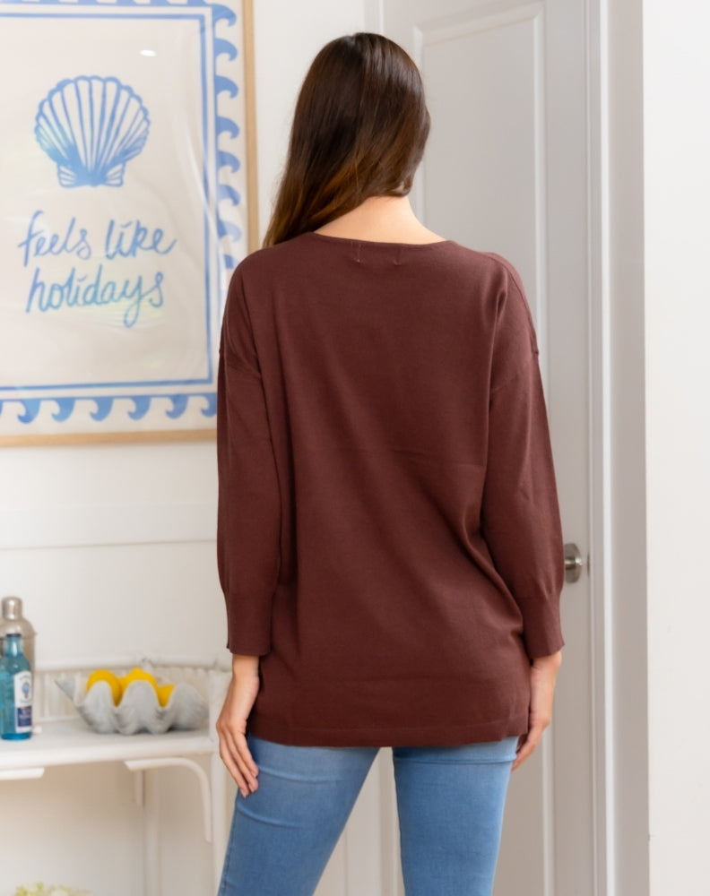 Woman wearing a brown sweater in a room with a decorative wall sign.