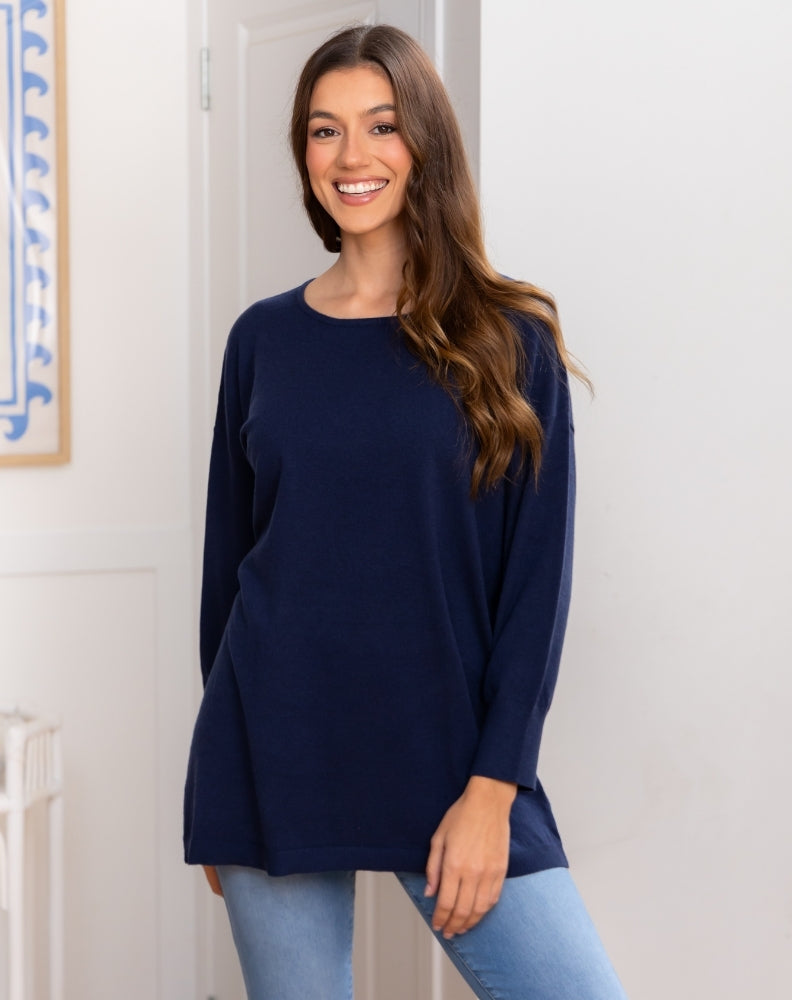 Woman wearing a navy blue long-sleeve top and light blue jeans indoors.
