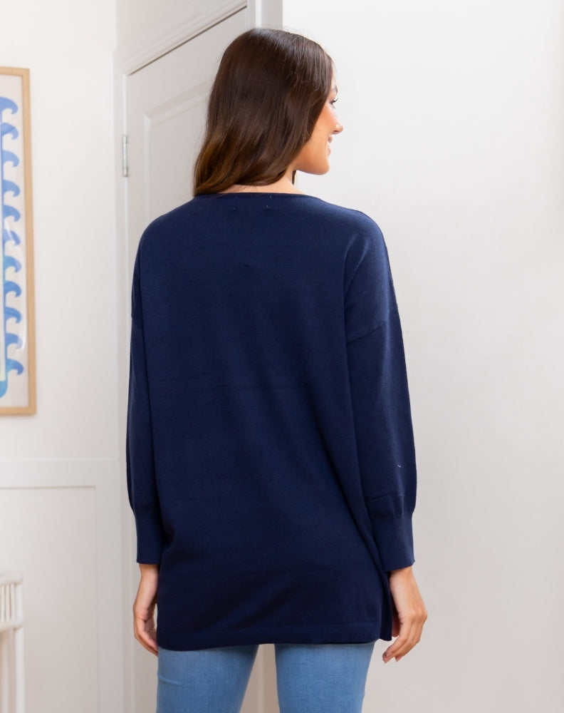 Woman wearing a navy sweater standing in a room with a white wall and a framed picture.