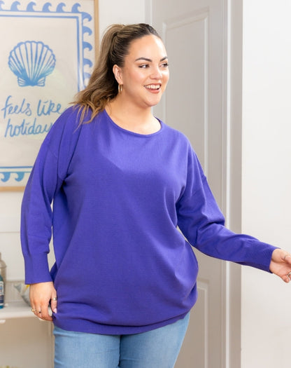 Woman wearing a purple tunic knit in a room with a decorative shell wall art.