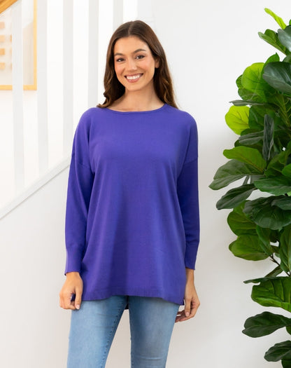 Woman wearing a purple long-sleeve top standing next to a green plant indoors.
