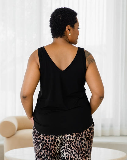 Person wearing a black sleeveless top and leopard print pants in a room with white curtains.