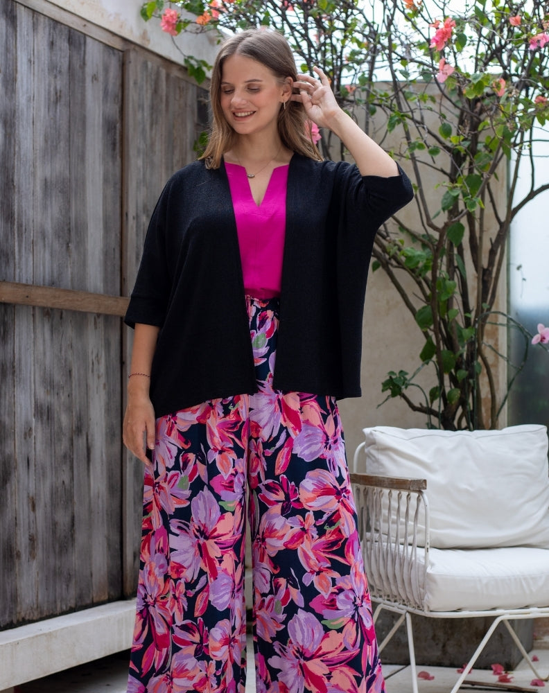 Woman wearing a black cardigan, pink top, and floral skirt in an outdoor setting.