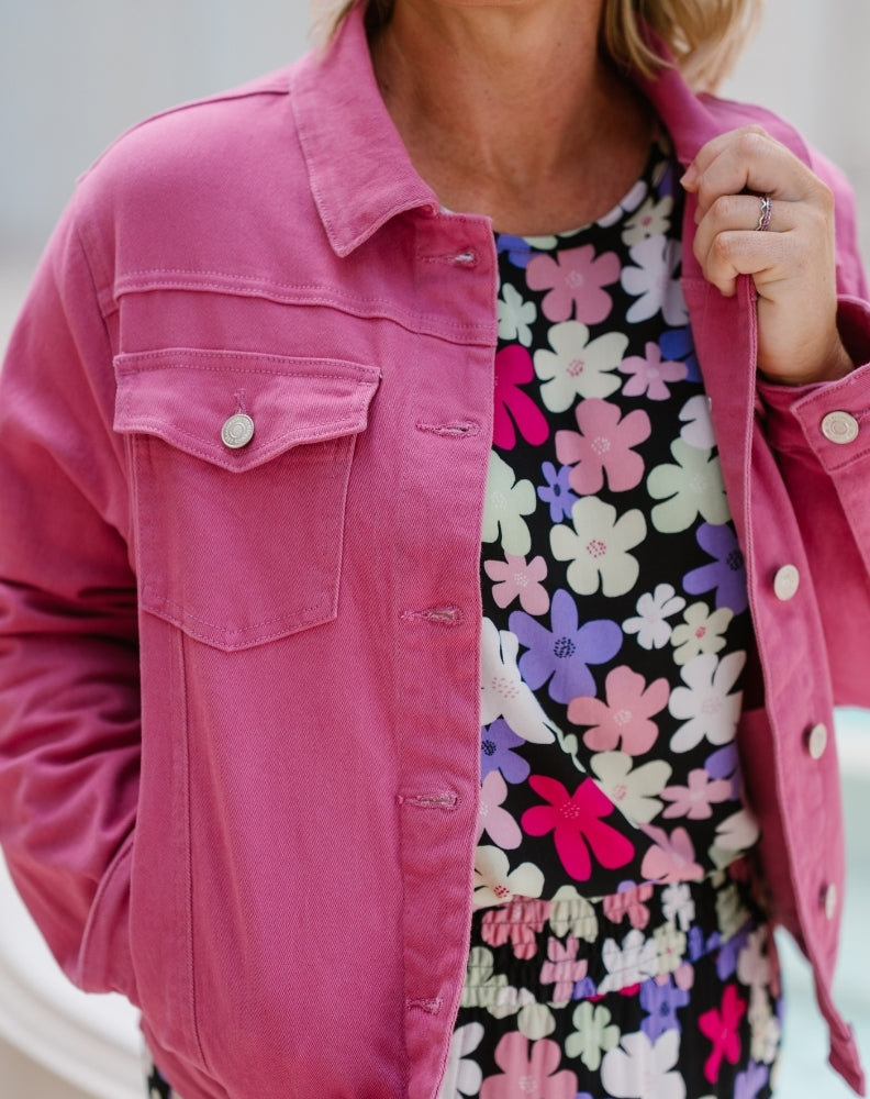 A close-up of a person wearing a bright pink denim-style jacket over a black floral top with pink, purple, and white flowers.
