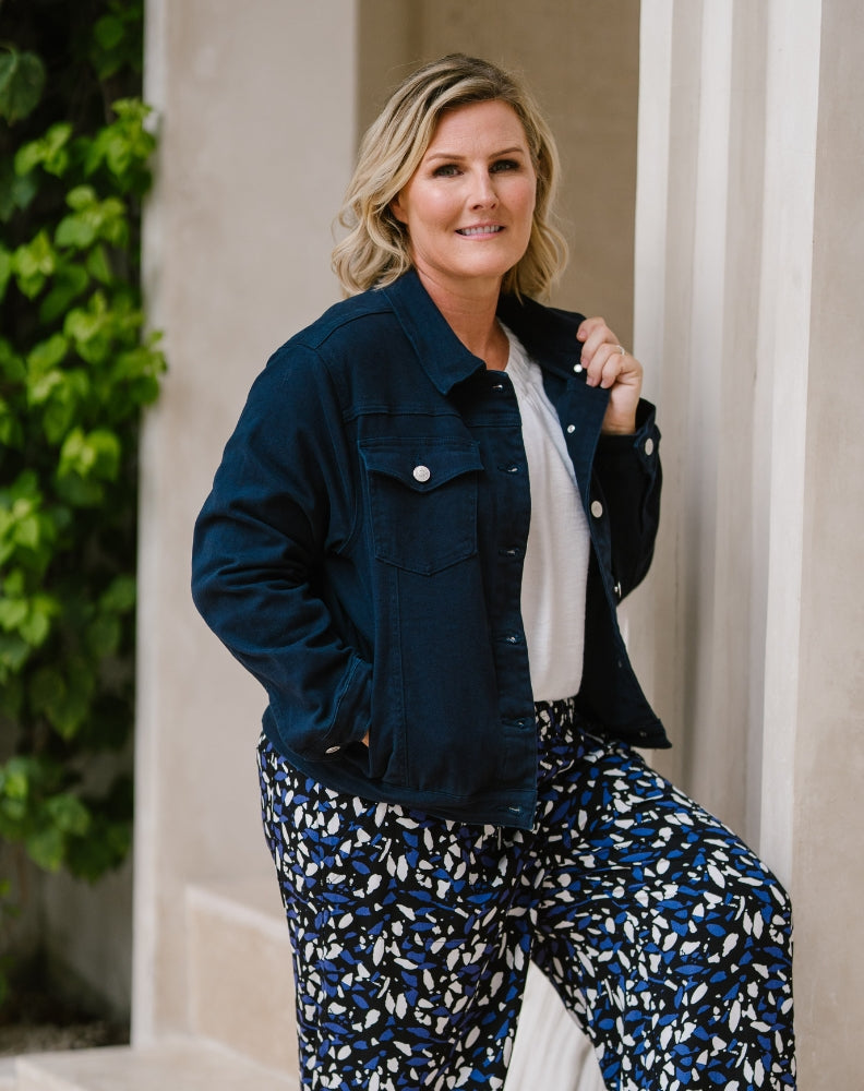 A woman posing outdoors in a dark navy blue denim jacket, a white top, and blue, white, and black patterned pants.