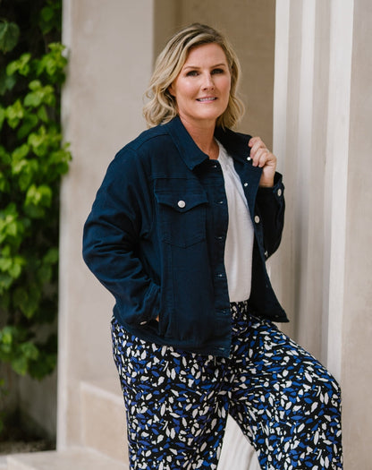 A woman posing outdoors in a dark navy blue denim jacket, a white top, and blue, white, and black patterned pants.