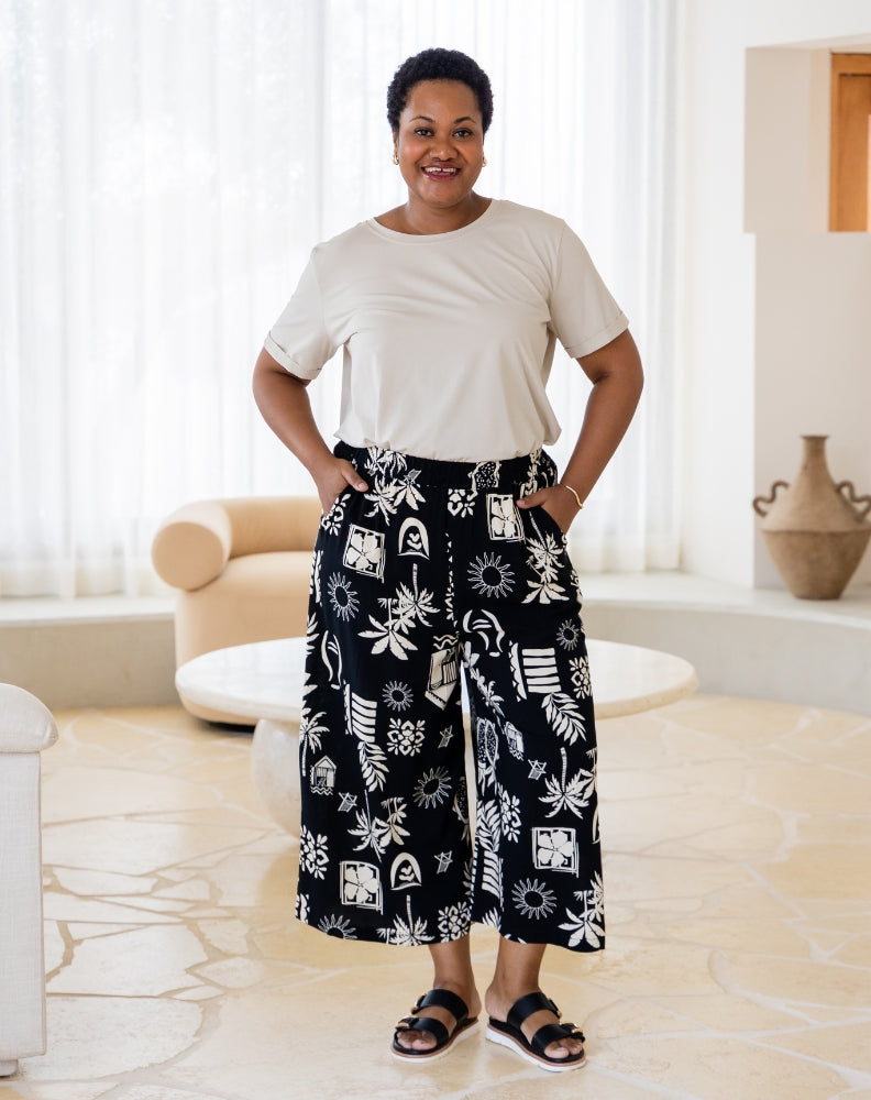 Woman wearing a white top and black patterned pants standing in a bright room.