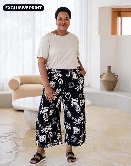 Woman wearing a white top and black patterned pants in a living room.