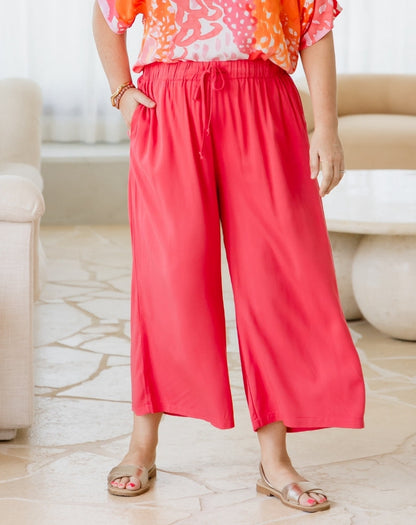 Person wearing a colorful top and red wide-leg pants in a living room setting.