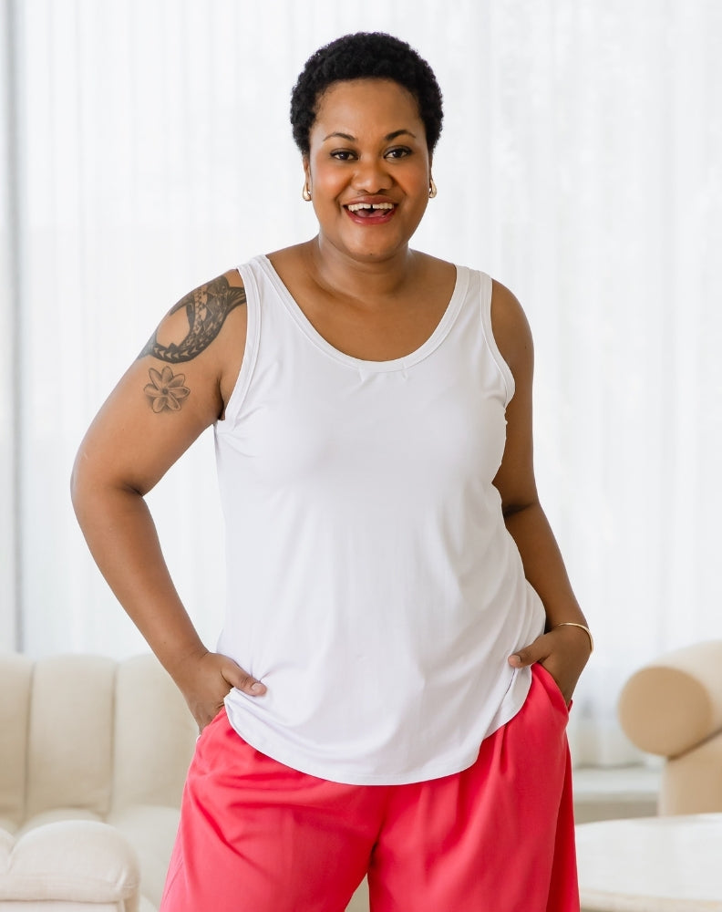 Woman wearing a white tank top and pink pants standing in a bright room.