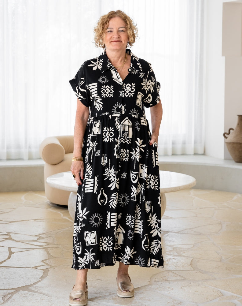 Woman wearing a black dress with white patterns in a room with light-colored flooring and decor.