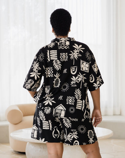 Person wearing a black shirt with white patterns in a room with white curtains and a beige chair.