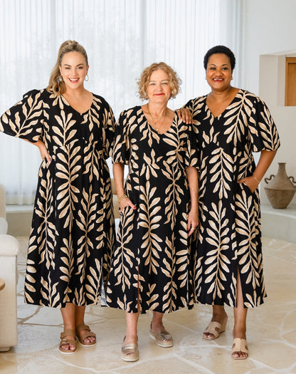 Three women wearing matching black and beige patterned dresses in a bright room.