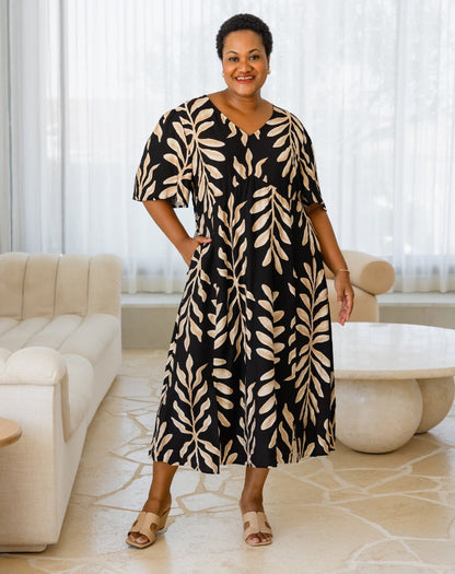 Woman wearing a black and beige leaf-patterned dress in a modern living room.