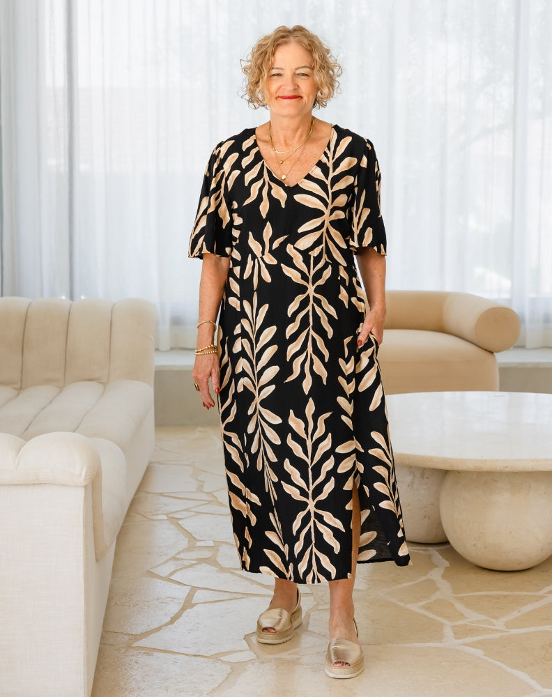 Woman wearing a black dress with beige leaf pattern in a modern living room.