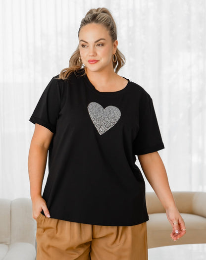 Woman wearing a black t-shirt with a silver heart design against a white curtain background