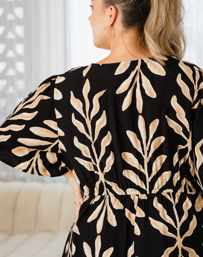 Woman wearing a black dress with beige leaf pattern indoors.