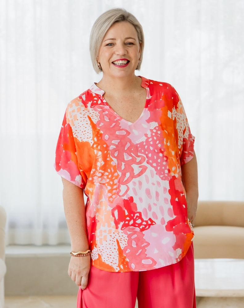 Woman wearing a colorful blouse with abstract patterns in a bright room.