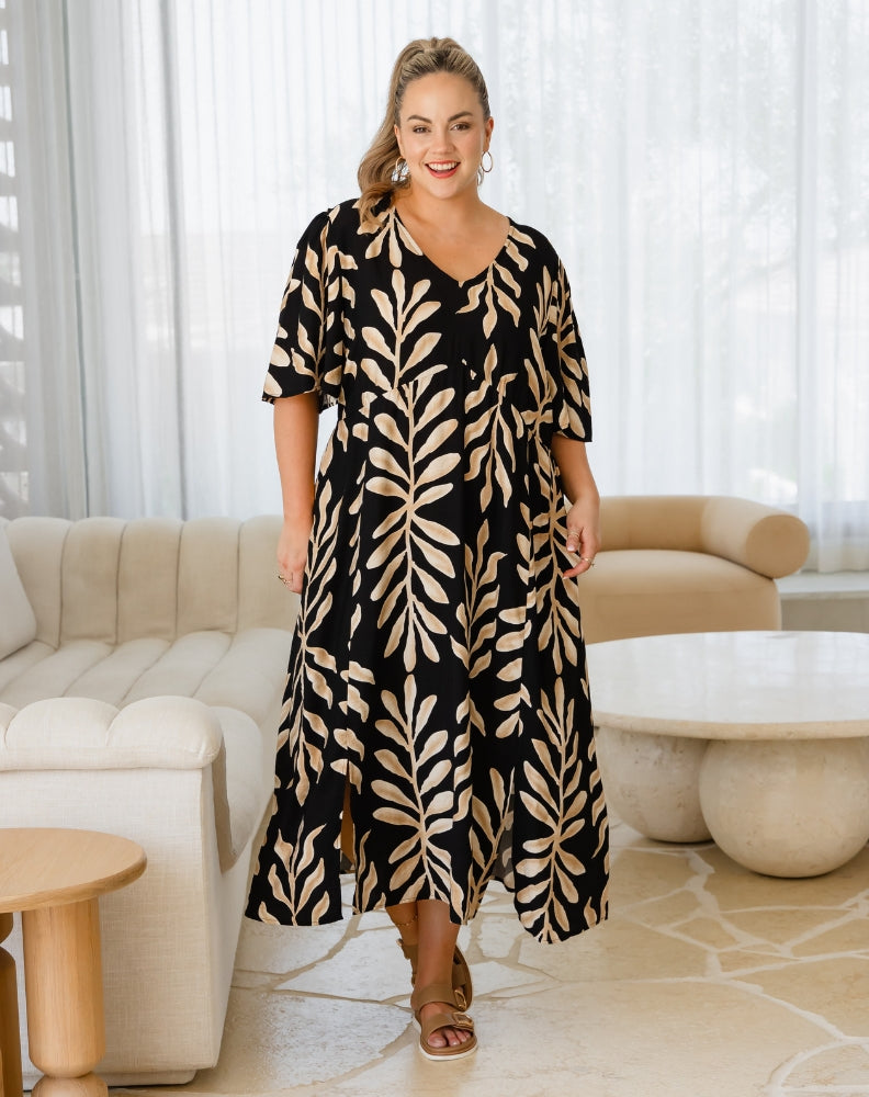 Woman wearing a black and beige leaf-patterned dress in a living room.