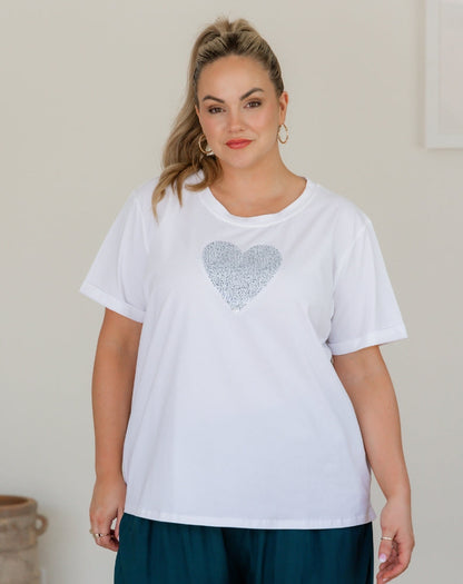 Woman wearing a white t-shirt with a silver heart design against a plain background