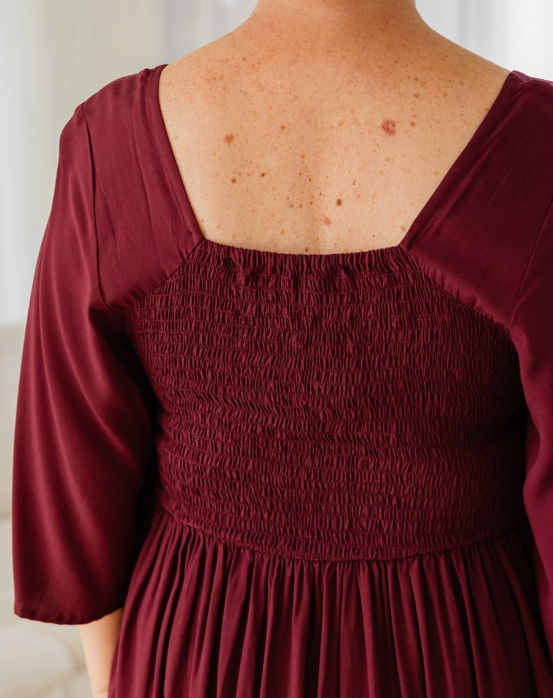 Maroon dress with smocked bodice and long sleeves on a neutral background
