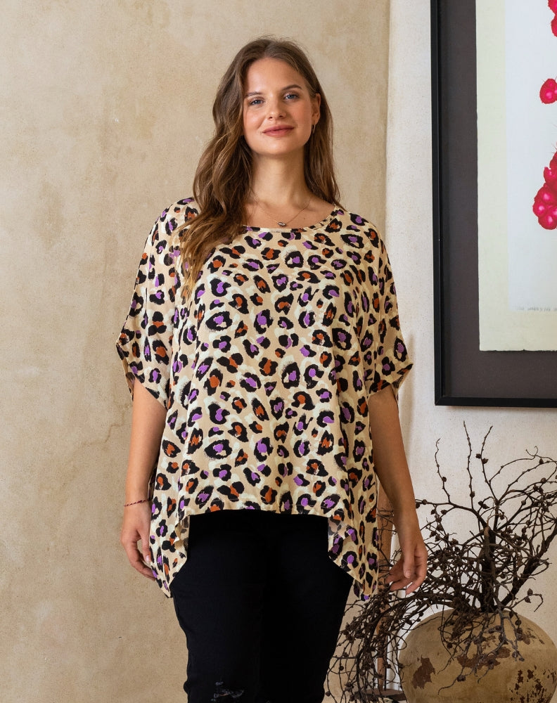 Woman wearing a leopard print top standing indoors with a neutral wall and decorative elements in the background.