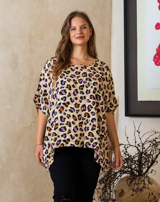 Woman wearing a leopard print top standing indoors with a neutral wall and decorative elements in the background.