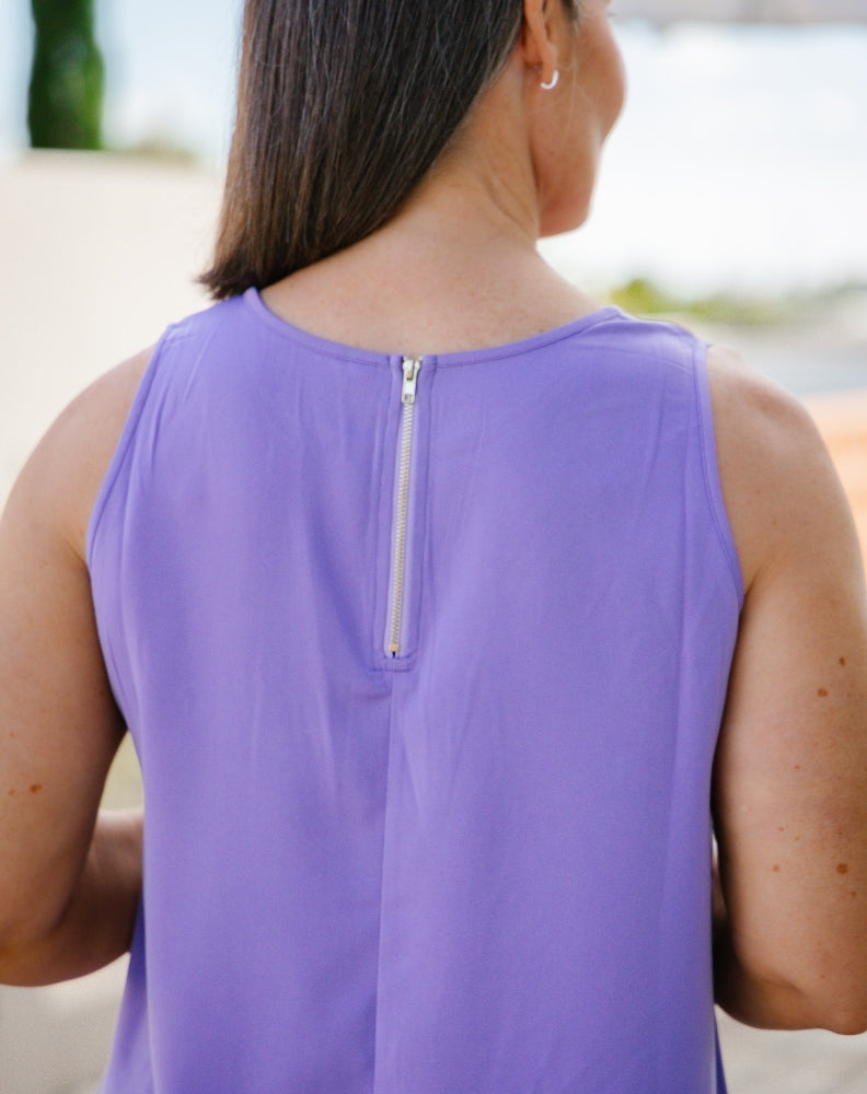 A woman viewed from the back wearing a sleeveless lavender-purple top with a silver zipper at the neckline.