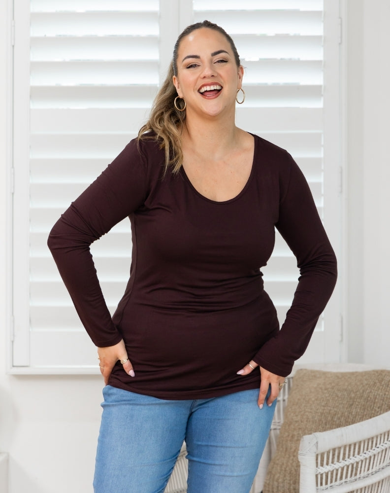 Woman wearing a brown long-sleeve top and blue jeans indoors.