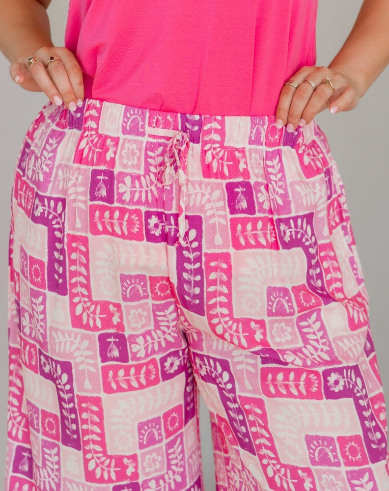 Person wearing pink and white patterned pants with a pink top against a gray background