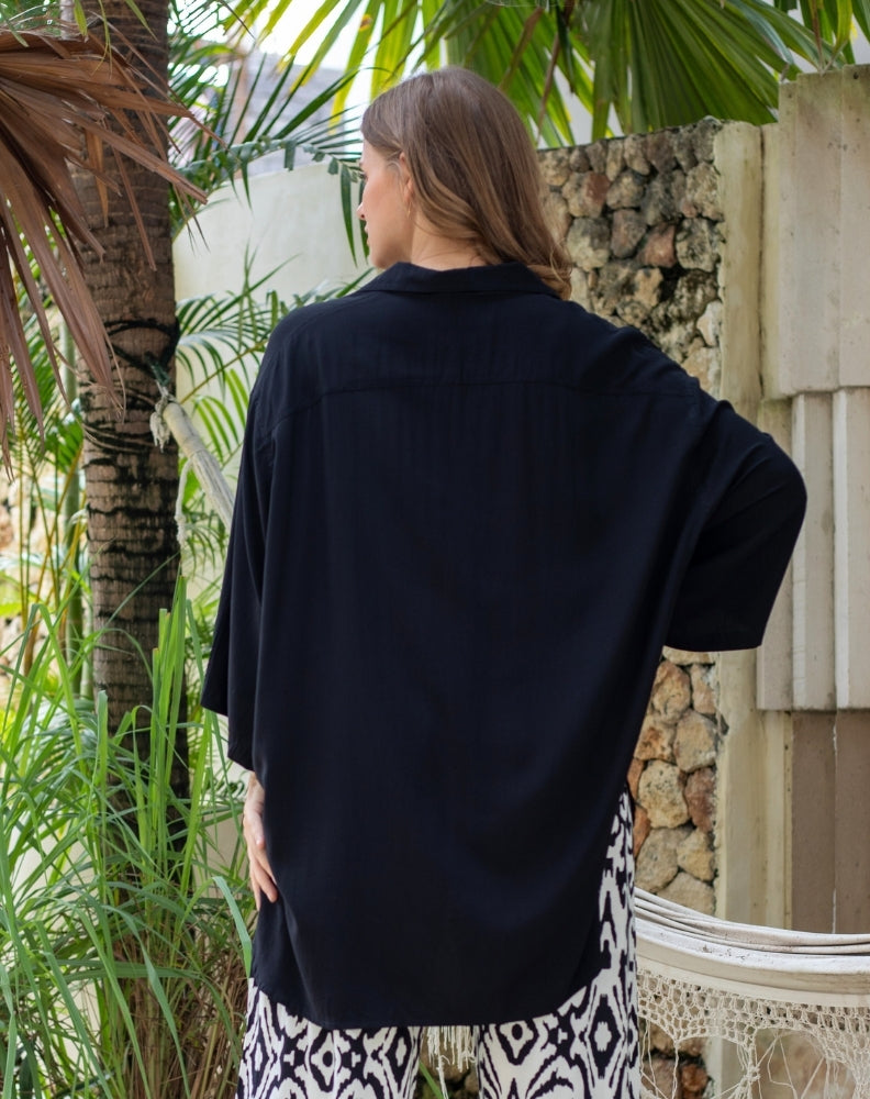 Person wearing a black shirt with a patterned skirt in a tropical setting