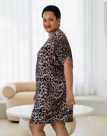 Woman wearing a leopard print dress in a room with white curtains and a beige chair.
