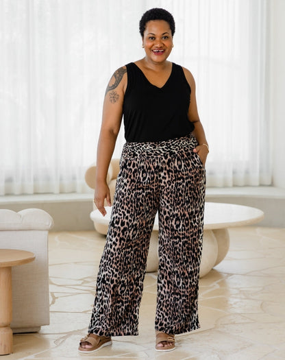 Woman wearing a black sleeveless top and leopard print pants in a room with white curtains.