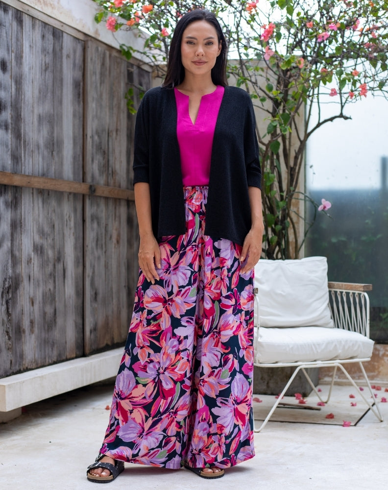 Woman wearing a black cardigan, pink top, and floral pants in an outdoor setting.