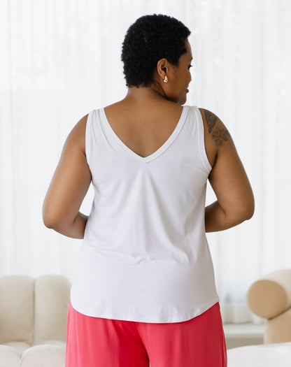 Person wearing a white tank top and pink pants in a room with a white couch and light-colored walls.